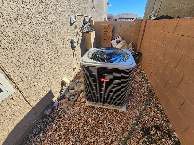 Outdoor AC condenser in a Tucson side yard with gravel, stucco wall, and service disconnect